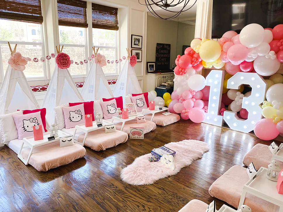 Guirnalda de globos coral, rosa y blanco junto a números con luces en una pijamada con teepees