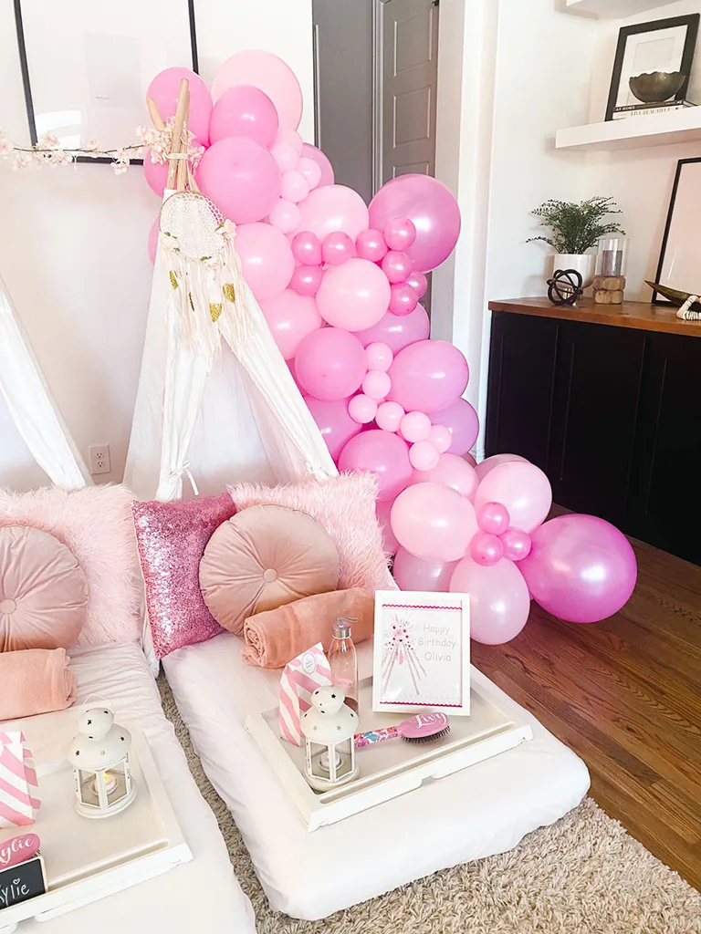 Guirnalda de globos rosa enmarcando un teepee blanco con almohadones rosa pálido
