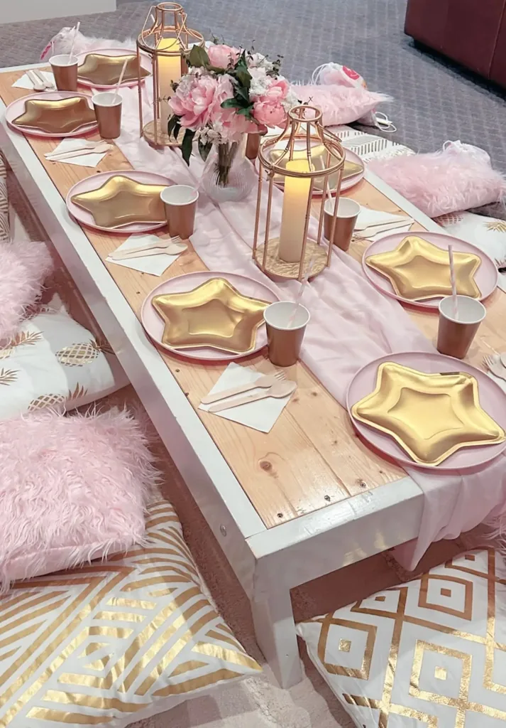 Mesa de picnic de lujo decorada en rosa y dorado con flores y cubiertos para cada invitado