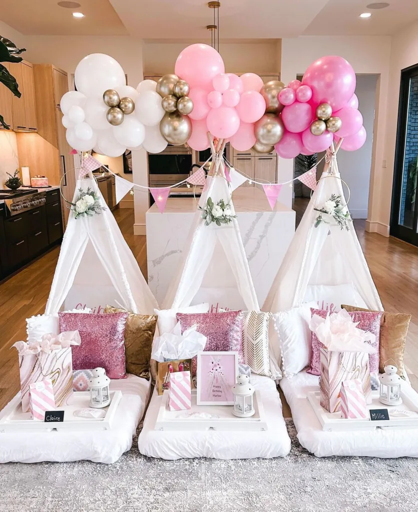 Nubes de globos rosa, dorado y blanco sobre tres teepees decorados