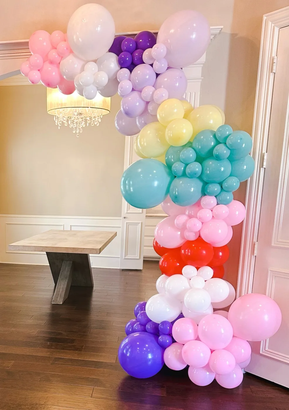 Guirnalda de globos en tonos pastel, rosa, lila, amarillo y aqua, enmarcando una puerta