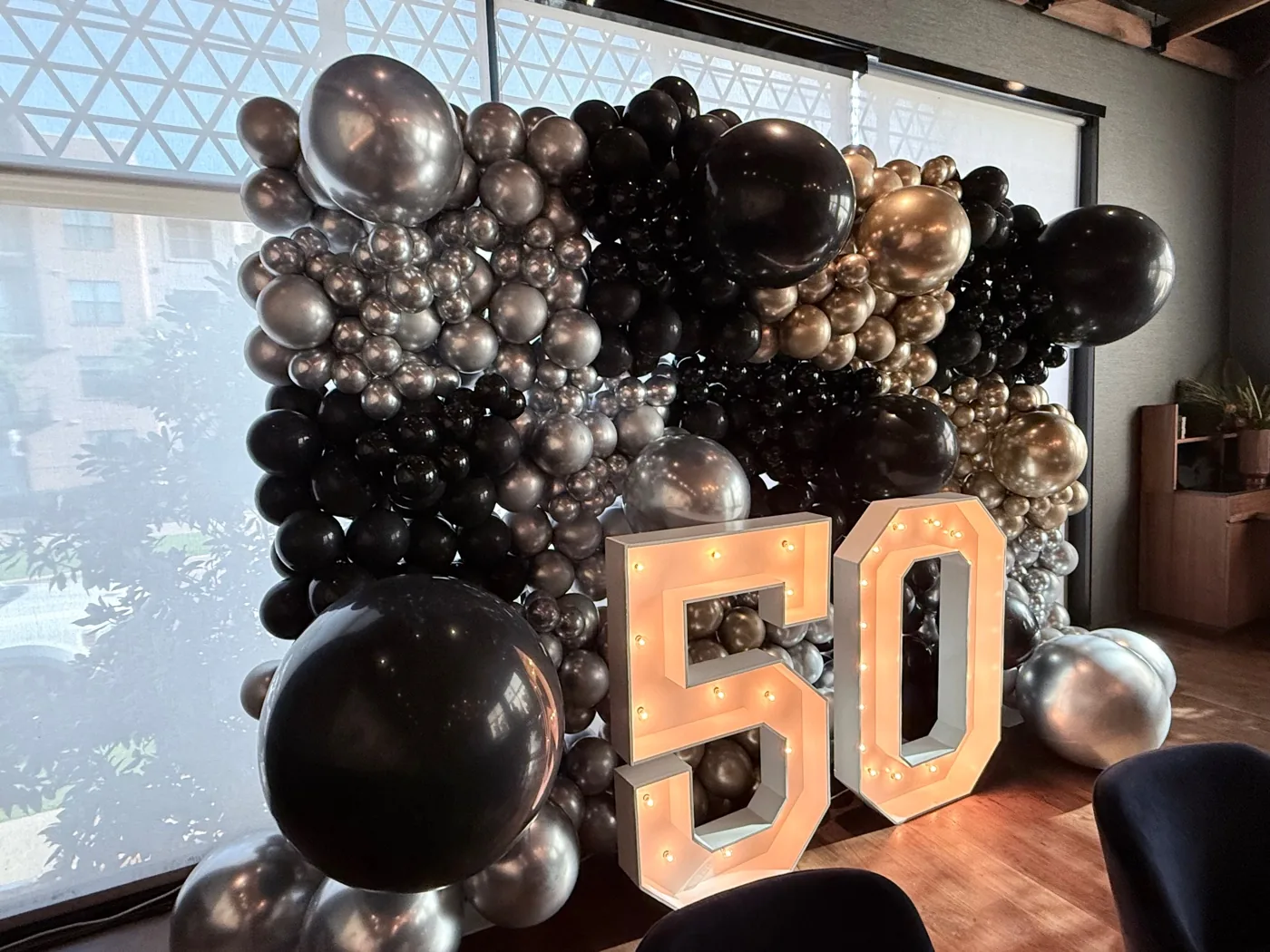 Pared de globos plateados, dorados y negros con el número 50 iluminado
