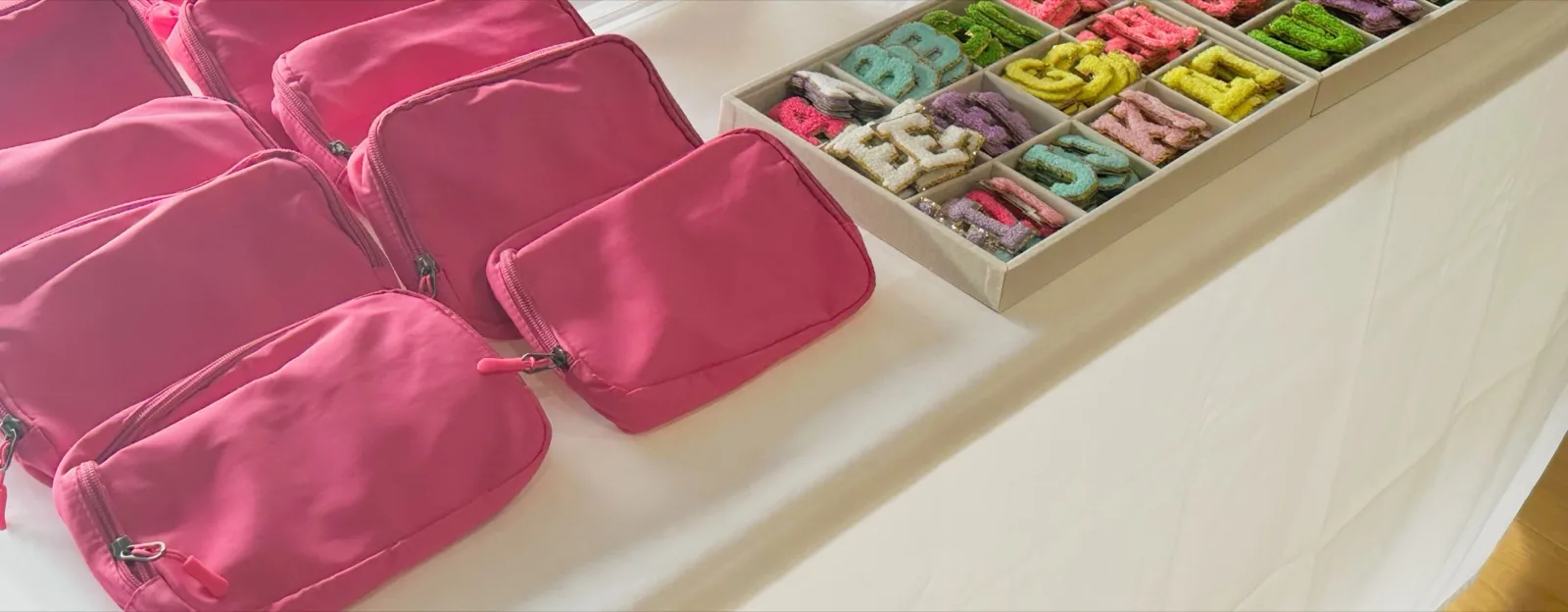 Pink fanny packs lined up next to a tray of letter patches