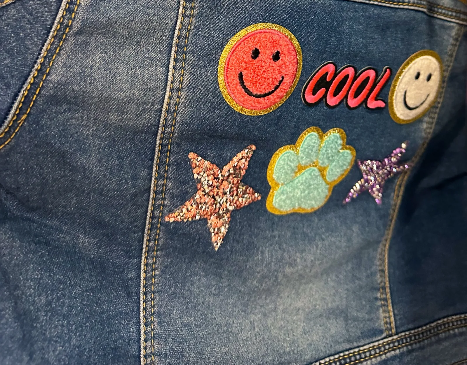 Back of a denim jacket with smiley faces, a paw print and glitter star patches