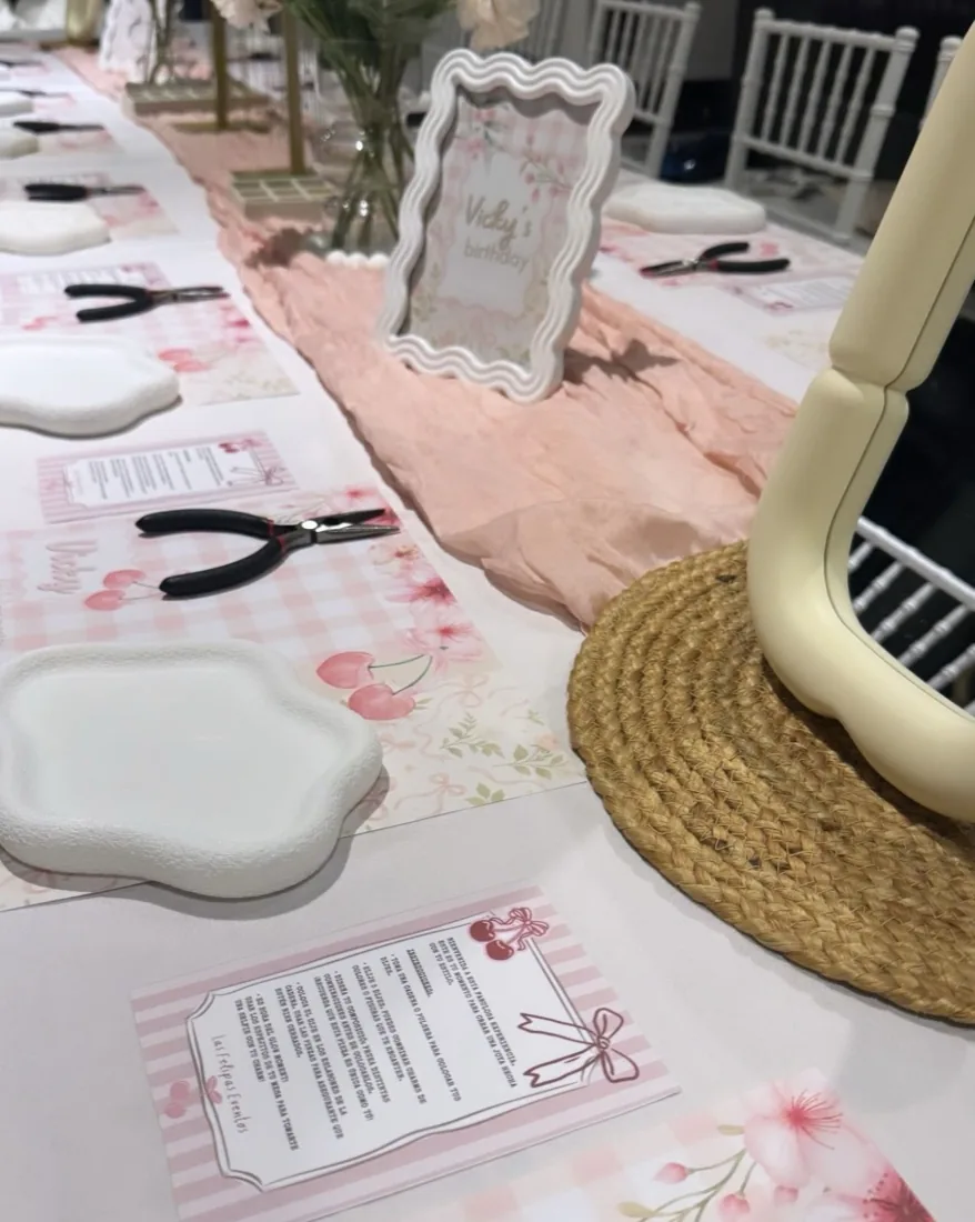 Long jewelry workshop table set with pliers, trays, pink placemats and flowers