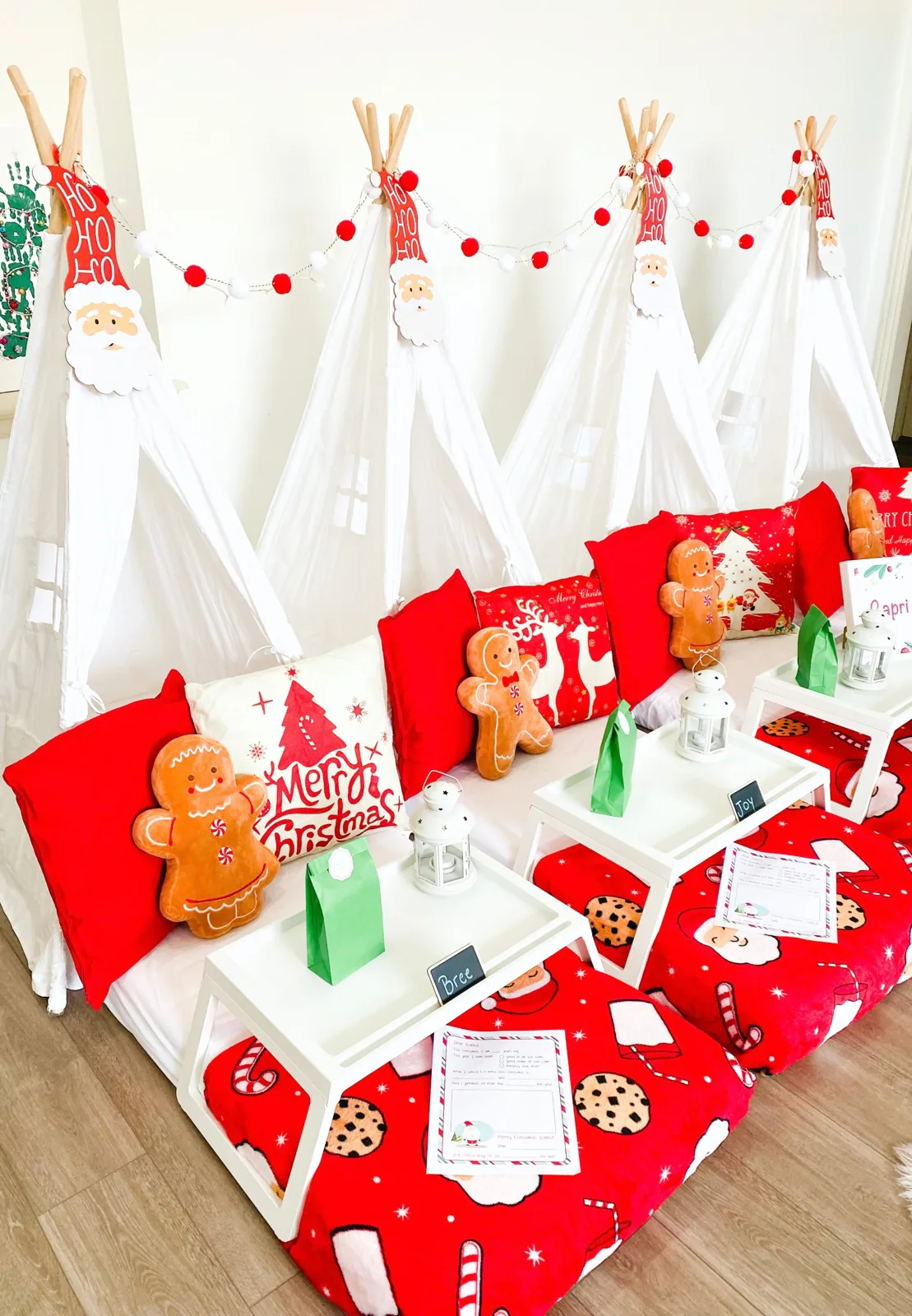 Four white teepees styled for Christmas with Santa toppers, gingerbread pillows and lanterns