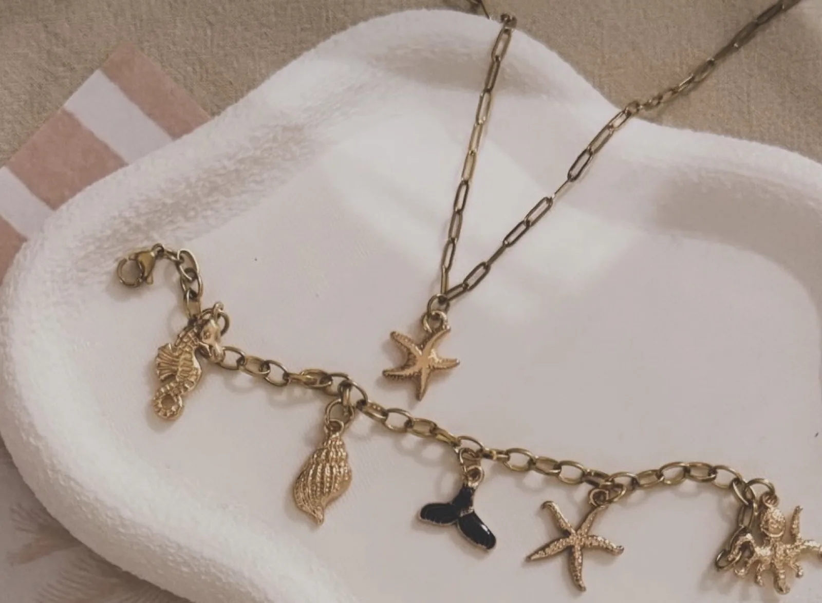 Gold charm bracelet with shells and starfish beside a gold starfish necklace on a white tray