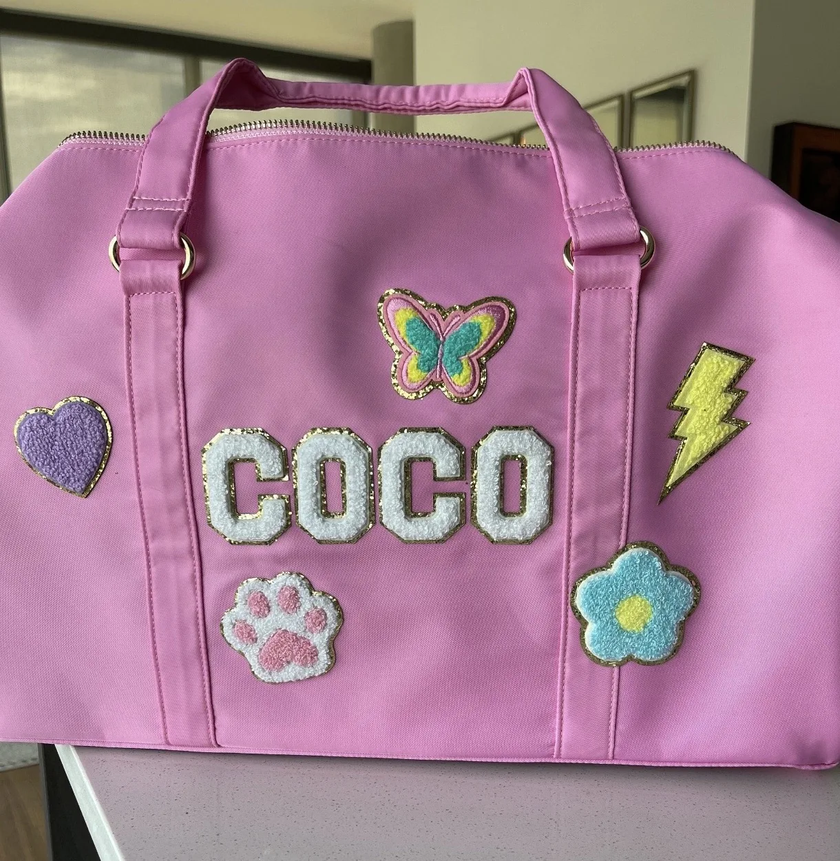 Pink duffel bag personalized with a name, a butterfly, a heart, a paw print, a flower and a lightning bolt
