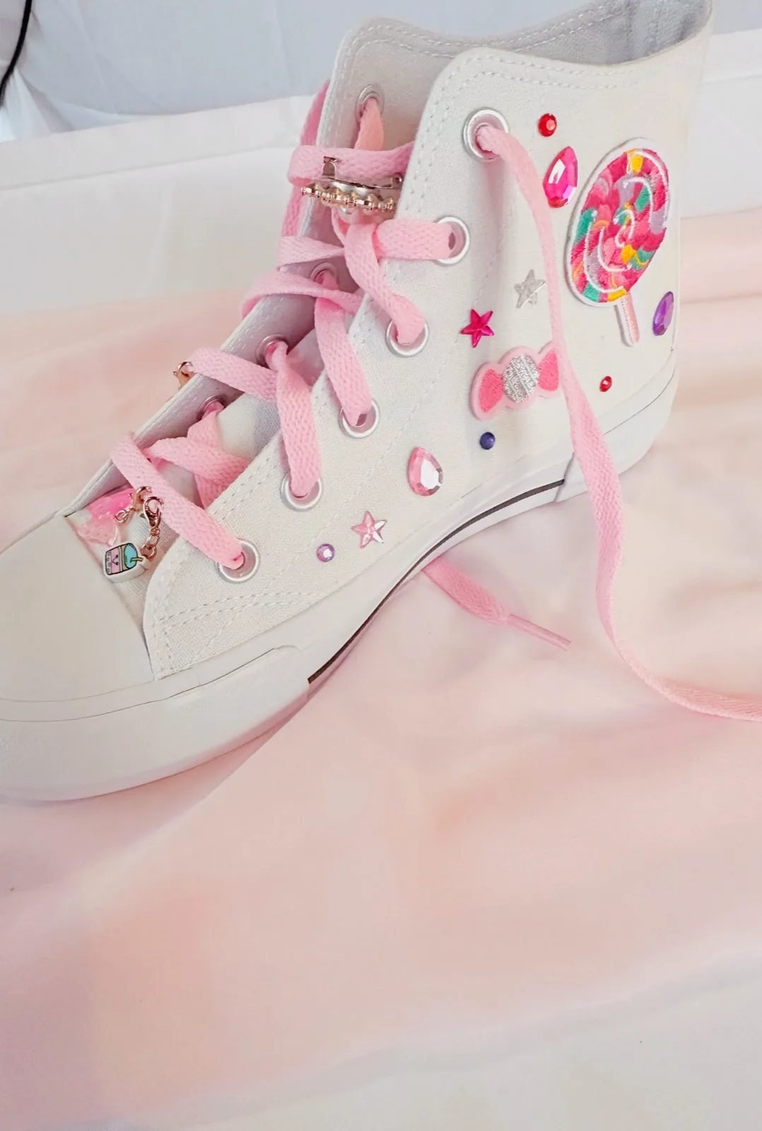 White canvas high top sneaker decorated with a lollipop patch, gems and pink laces