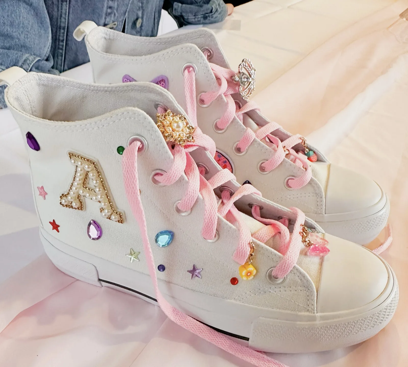 White canvas sneakers decorated with a pearl letter patch, gems and pink laces